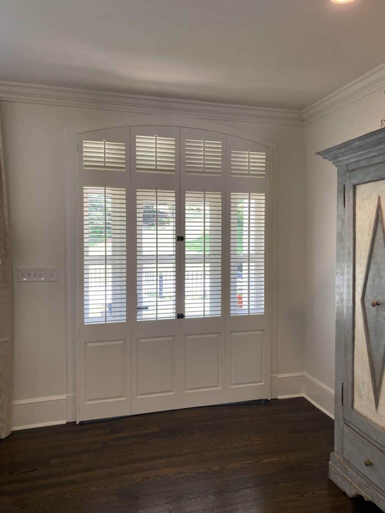 Bi-folding arched doorway with traditional paneled and louvered shutters.